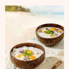 A bowl of coconut soup served in a natural coconut shell bowl with a wooden spoon on a light background.