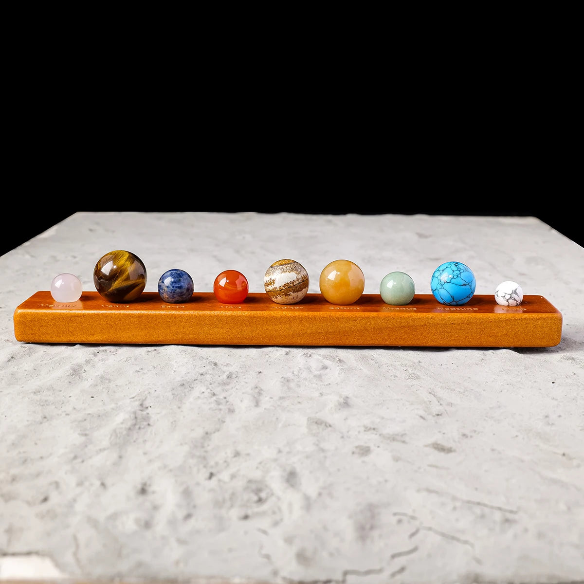 A set of natural crystal solar system planet balls arranged in a row on an orange wooden base.