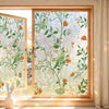 A close-up of a window featuring decorative privacy film with green and orange floral patterns.