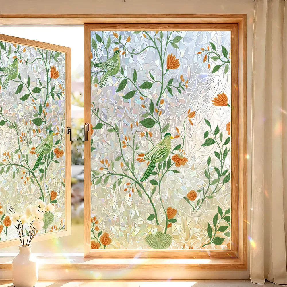 A close-up of a window featuring decorative privacy film with green and orange floral patterns.