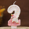 Una vela blanca con forma de 9 decorada con purpurina y una pequeña figura de unicornio rosa.