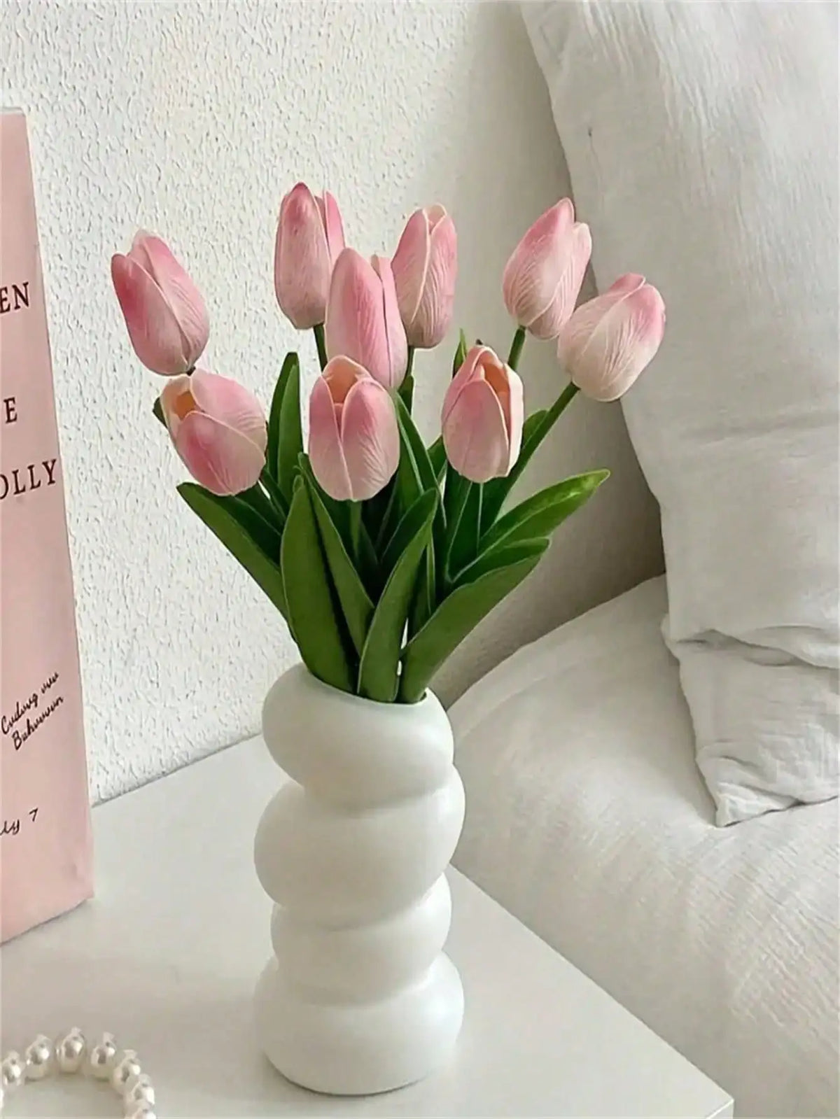 A bouquet of six pink tulips in a white vase displayed on a white surface.