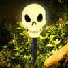 A white skull light fixture with glowing eyes is displayed amidst green foliage.