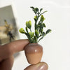 A hand holds a mini ceramic vase fridge magnet with artificial green flowers.