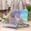 A set of iridescent holographic gift bags with sturdy handles displayed next to a deer antler and pink tulips.