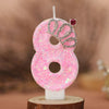 Pink glitter number eight birthday candle with a crown topper on a wooden stand