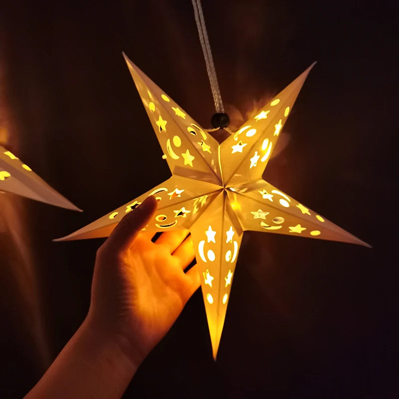 A hand holds up a glowing, star-shaped pendant light decorated with yellow stars against a dark background.
