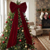 A decorated Christmas tree featuring a large red velvet bow with long streamers and ornaments.