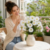 A woman smiles while holding a bouquet of white artificial silk cloth flowers on a table.