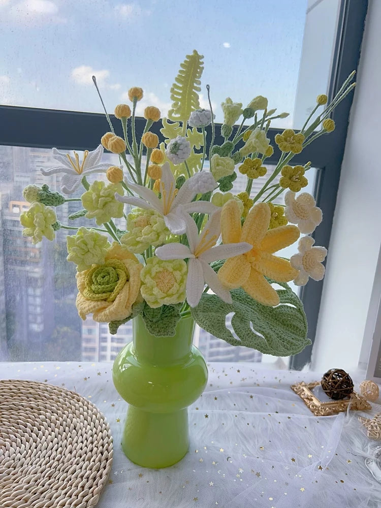 Un ramo de flores de ganchillo hecho a mano con flores amarillas y blancas y follaje, exhibido en una mesa.