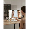A woman uses a tri-fold LED makeup mirror with dimmable lighting in a modern bathroom setting.