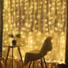 Golden fairy lights drape across a sheer curtain, illuminating a potted plant and a velvet chair.