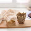 A small terracotta cup filled with crumpled newspaper style cupcake liners resting on a wooden board.