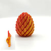 A close-up view of a 3D printed dragon egg fidget toy with textured orange and yellow scales.
