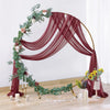 Arche en bois décorée de drapés de mousseline rouge profond et de feuillage vert pour fond d'événement.
