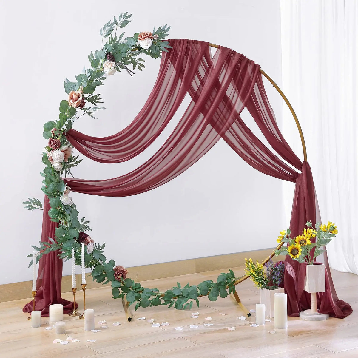 Arche en bois décorée de drapés de mousseline rouge profond et de feuillage vert pour fond d'événement.
