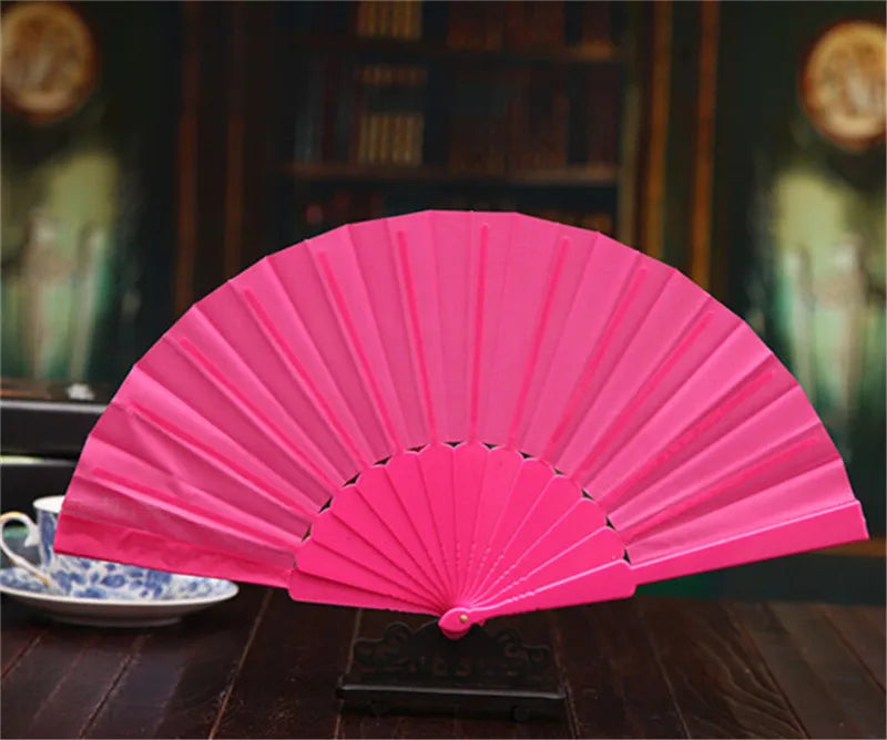 A bright pink lace folding hand fan displayed on a dark wooden surface.