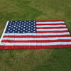 A large embroidered USA flag displayed outdoors on green grass.