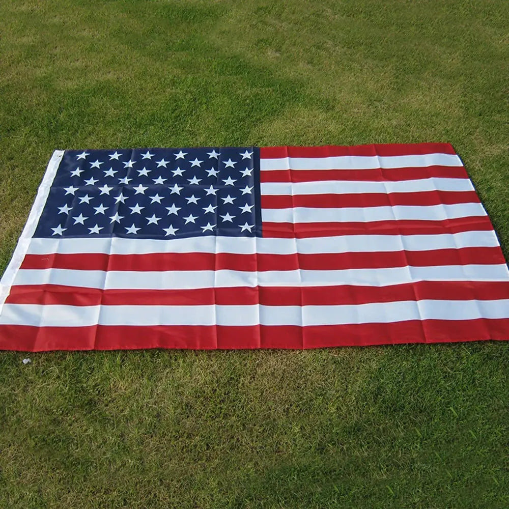 A large embroidered USA flag displayed outdoors on green grass.