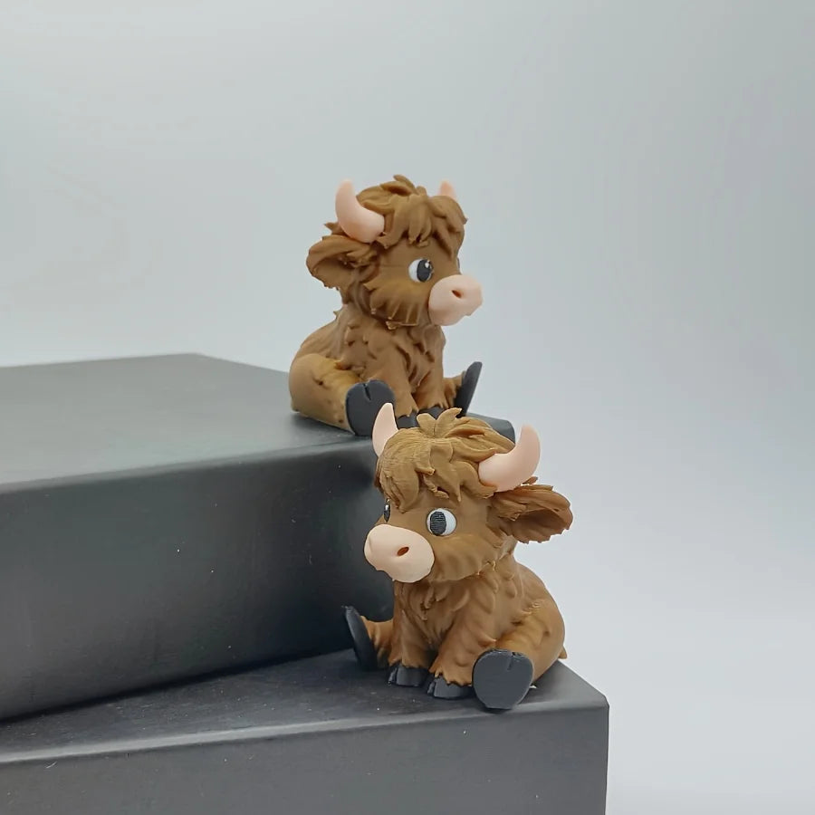 A small, brown Highland cow statue with horns sitting on a dark gray surface.