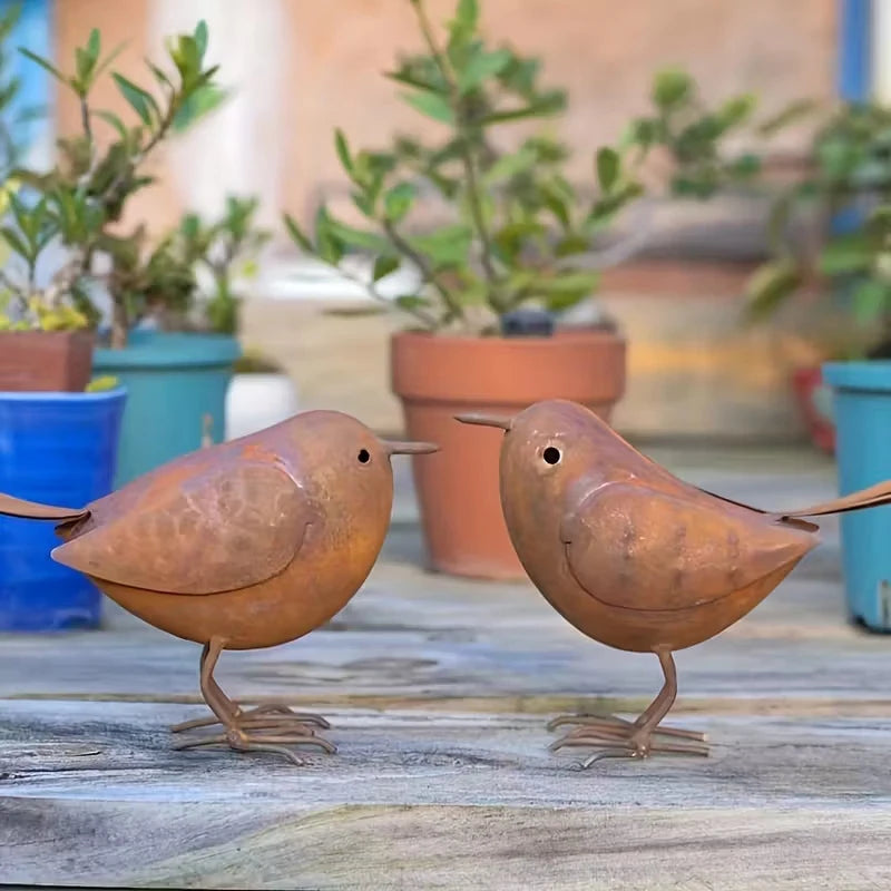 Two rustic metal bird sculptures in brown tones standing on weathered wood.