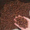 A hand holds a pile of brown foam beads for crafting and decoration.