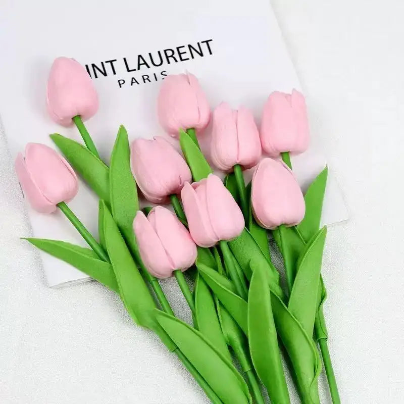 A bouquet of pink artificial tulips with green stems and leaves on a white background.