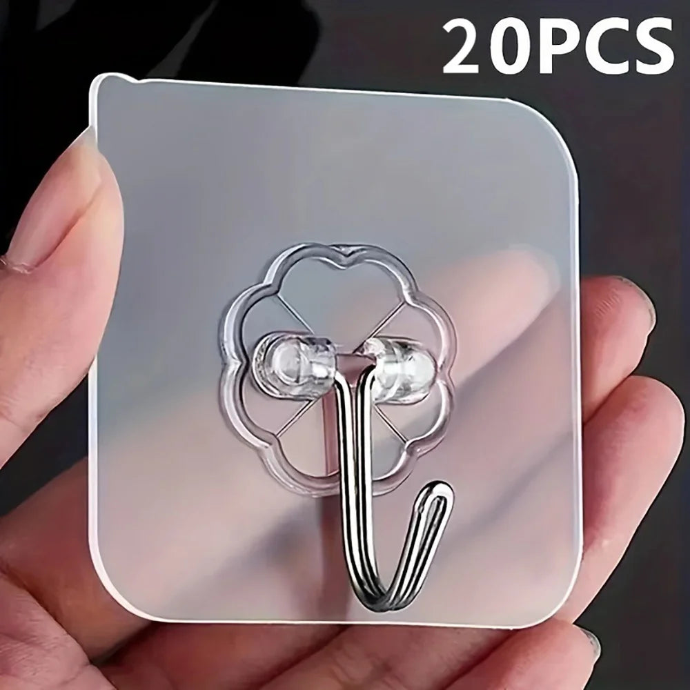 A clear adhesive wall hook with a silver hook is shown being held in a hand against a light background.