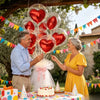 A man and a woman celebrate with heart-shaped foil balloons and bubble balloons outdoors.