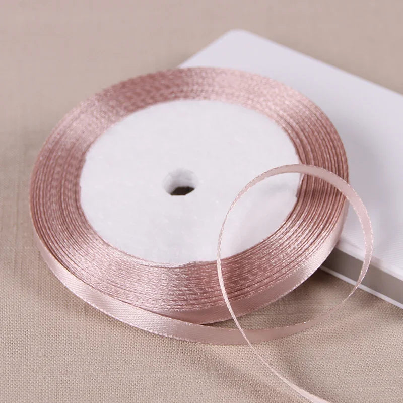 A roll of pink satin ribbon on a white spool resting on a light beige surface.