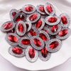 A pile of red gemstone flatback rhinestones with silver settings on a white surface.