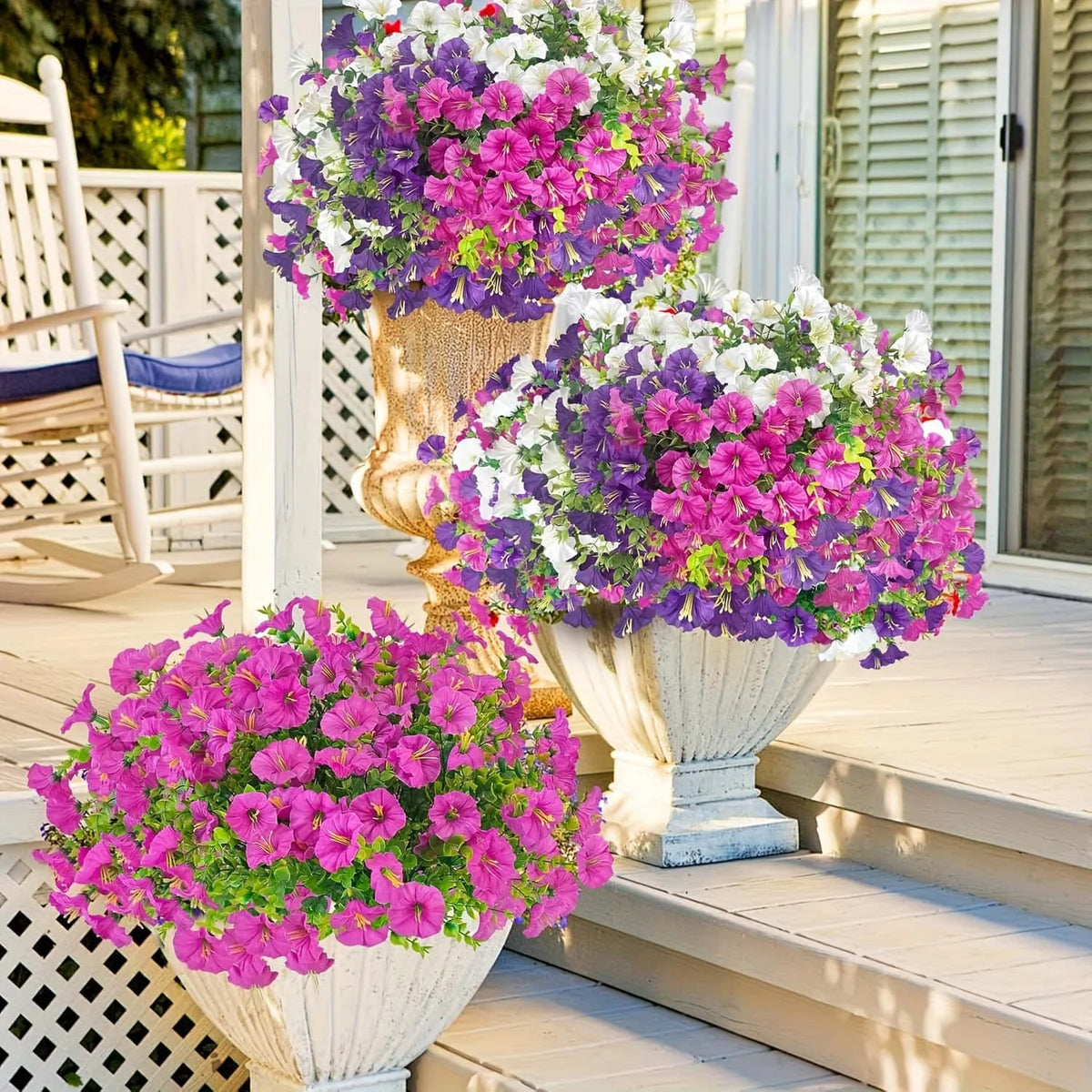 A display of colorful artificial flowers in pink, purple, and white blooms arranged in decorative planters on a wooden porch.