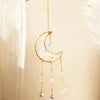 A handcrafted gold moon crystal suncatcher pendant hanging from a branch.