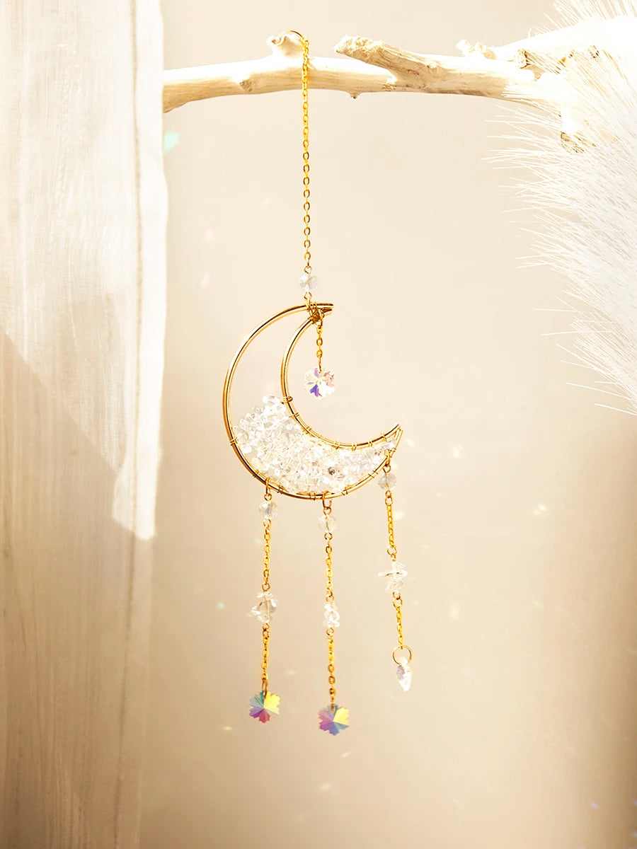 A handcrafted gold moon crystal suncatcher pendant hanging from a branch.