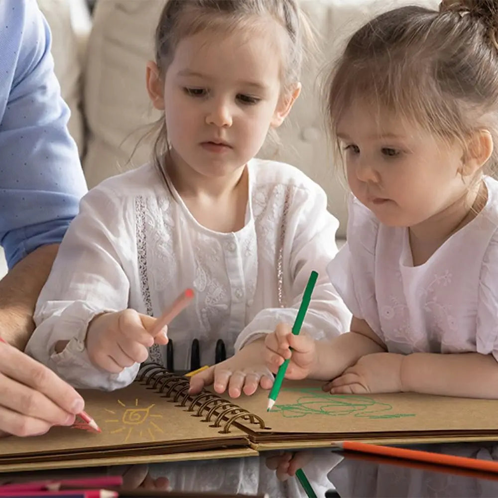Two young girls are writing in a handmade kraft paper scrapbook with colored pencils.