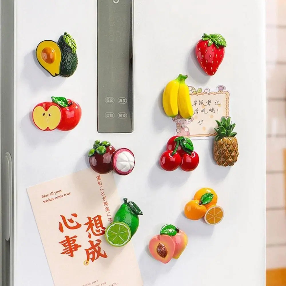 A white fridge featuring various colorful fruit magnets including strawberries, apples, and citrus slices.