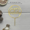 A gold acrylic cake topper with the words Happy Birthday on a thin stick, set against a light wooden background.