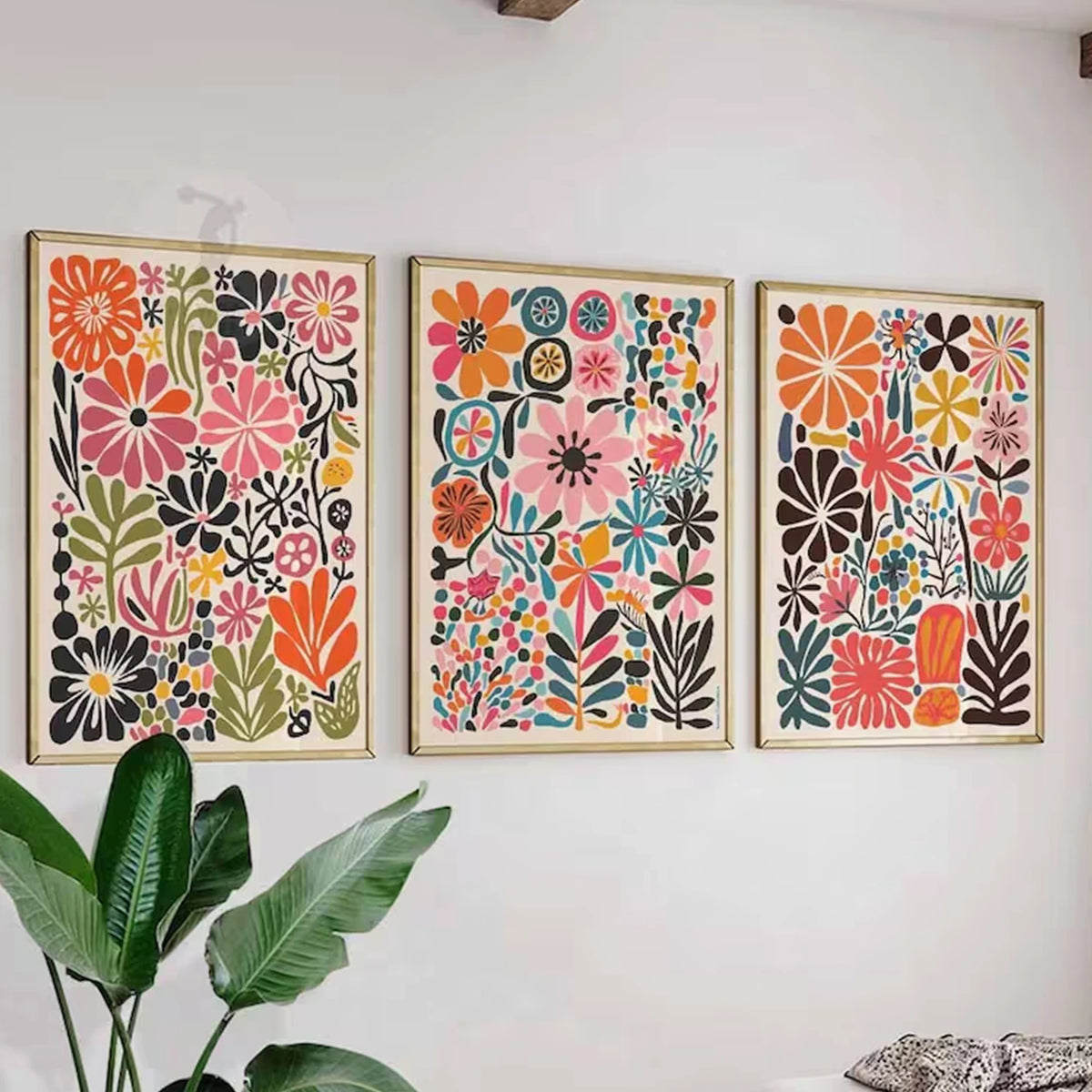 Tres impresiones florales botánicas enmarcadas con flores y follaje de colores en una pared blanca.