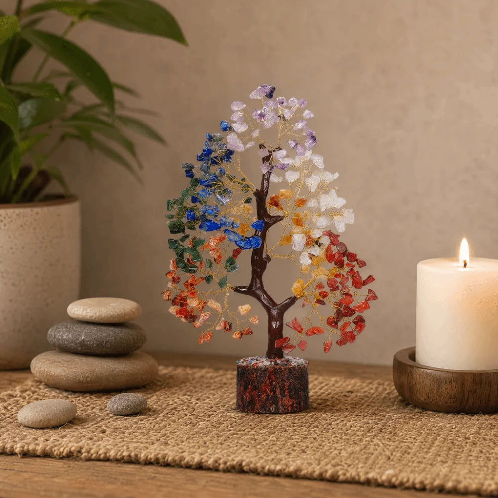 A bendable crystal tree ornament with colorful leaves stands on a wooden base next to a lit candle.