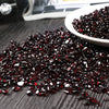 A pile of deep burgundy natural garnet crystal chips scattered on a dark surface with a small silver dish nearby.