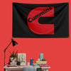 A black flag with the red letter C and the word Cummins printed on it, displayed on a red wall.