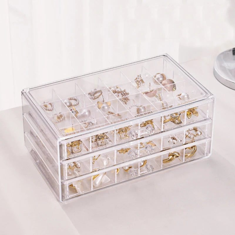 Clear acrylic jewelry organizer with three drawers filled with various gold and silver jewelry pieces