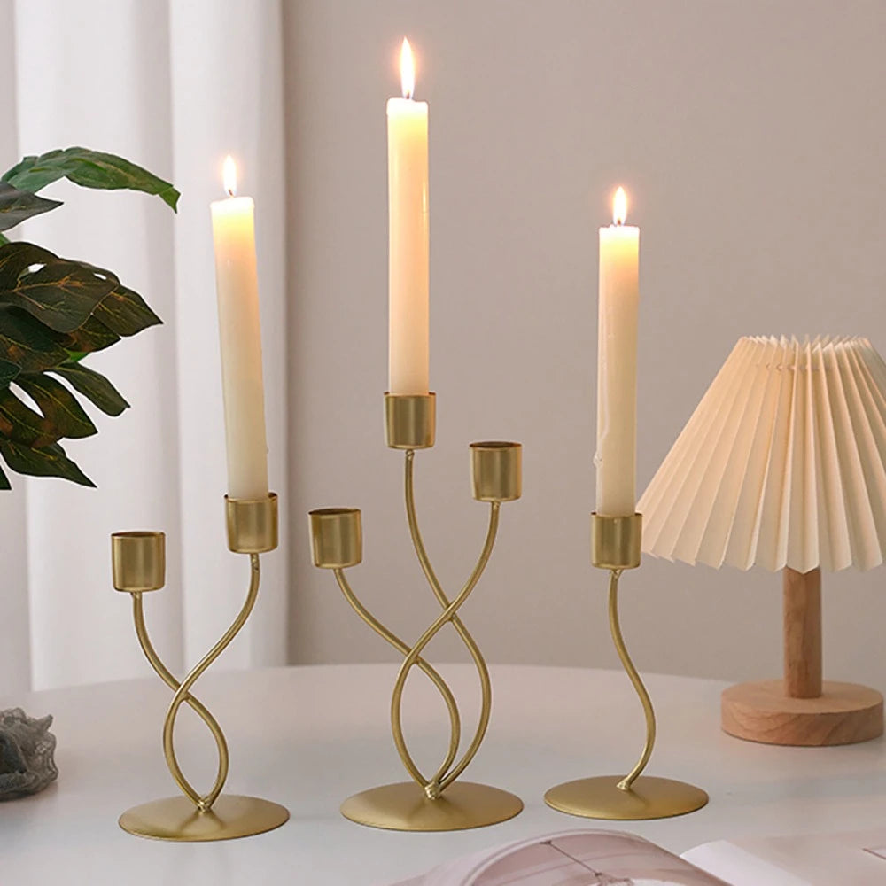 A set of elegant gold iron candle holders with white candles on a white table.