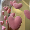 A hand holds a pink heart-shaped fabric curtain made of soft, fuzzy material hanging in the air.