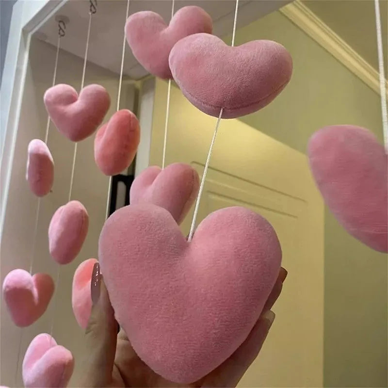 A hand holds a pink heart-shaped fabric curtain made of soft, fuzzy material hanging in the air.