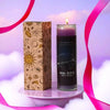A glass candle in a cardboard box featuring an Aries zodiac symbol, set against a purple and pink background.