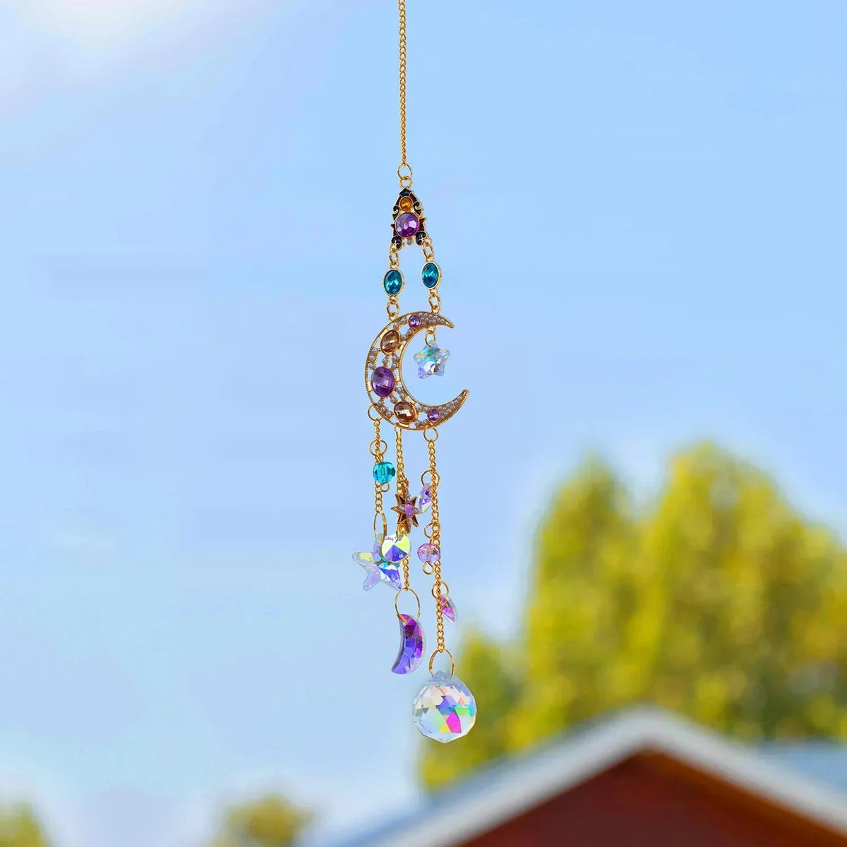 A delicate gold chain featuring purple and blue crystal rhinestone sun catchers hanging against a bright blue sky.