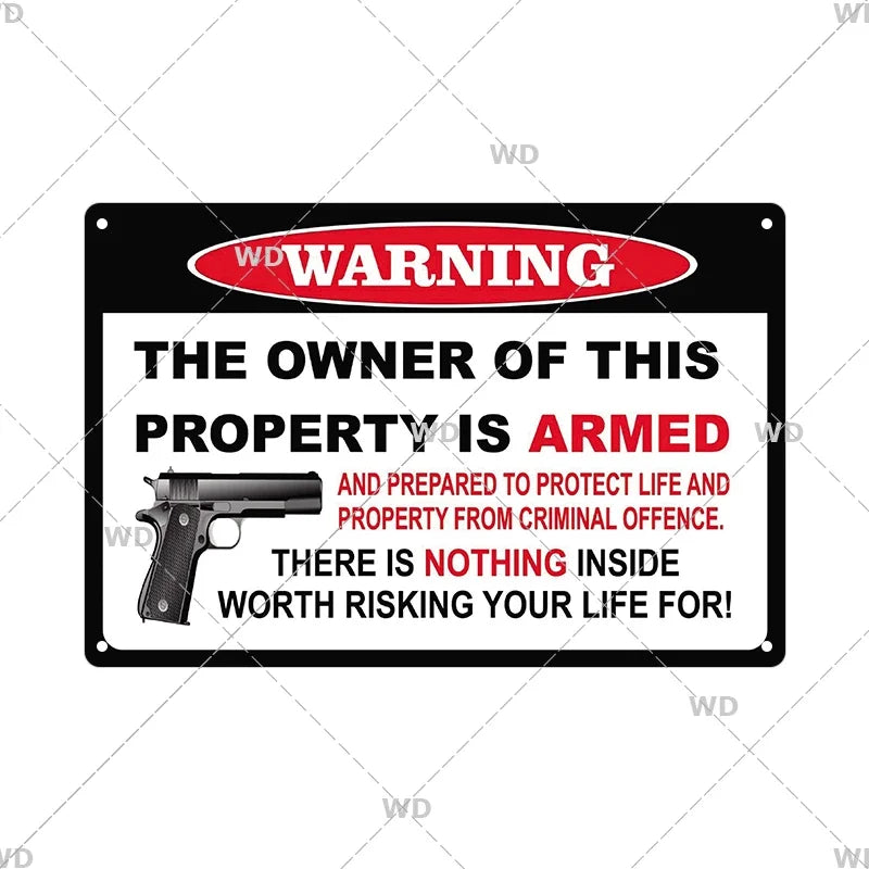 A black metal warning sign with yellow text stating that the owner of the property is armed and prepared to protect life and 