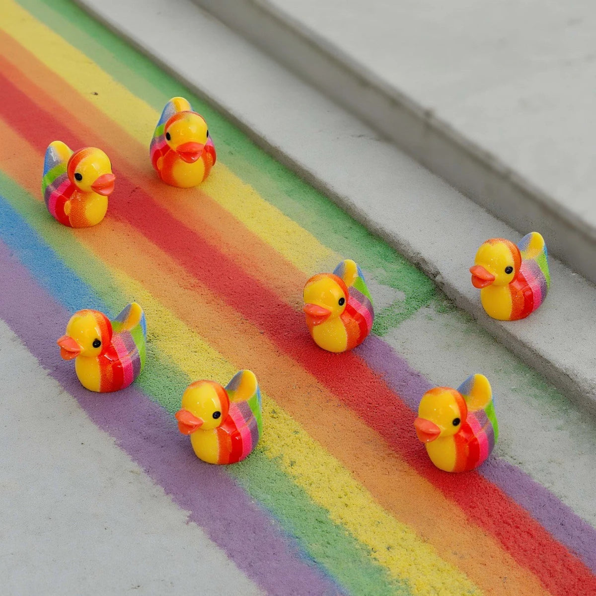 A set of mini resin colorful duck decorations arranged on a rainbow-colored background.
