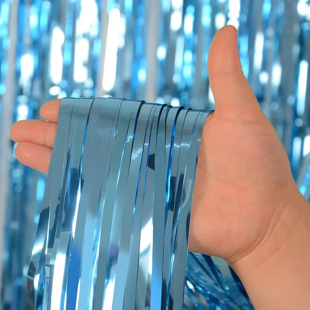 Une main tient des rideaux de franges iridescentes bleues, montrant la texture brillante et les filaments verticaux.